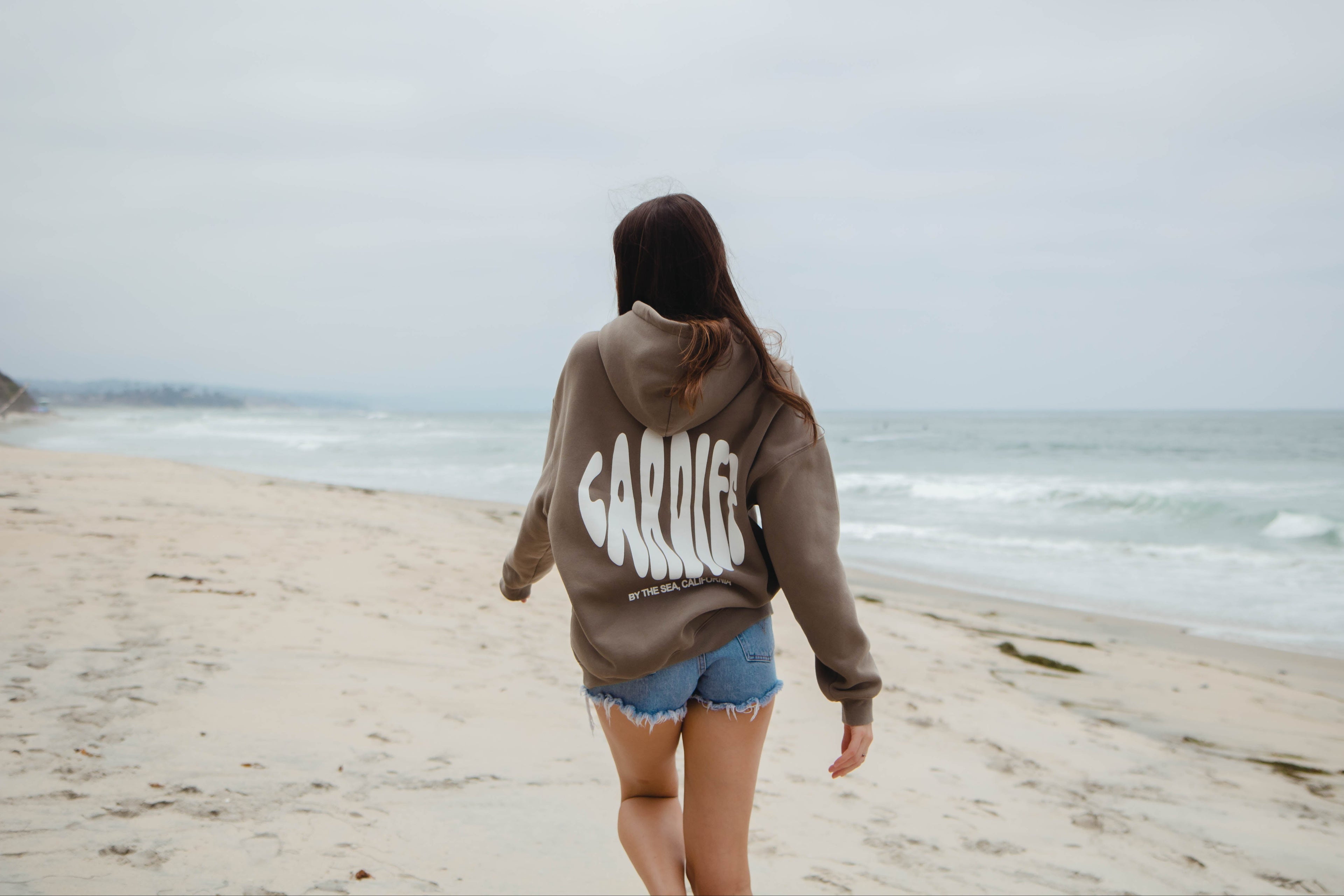 girl wearing a hoodie with 'Cardiff by the Sea, California' on a beach